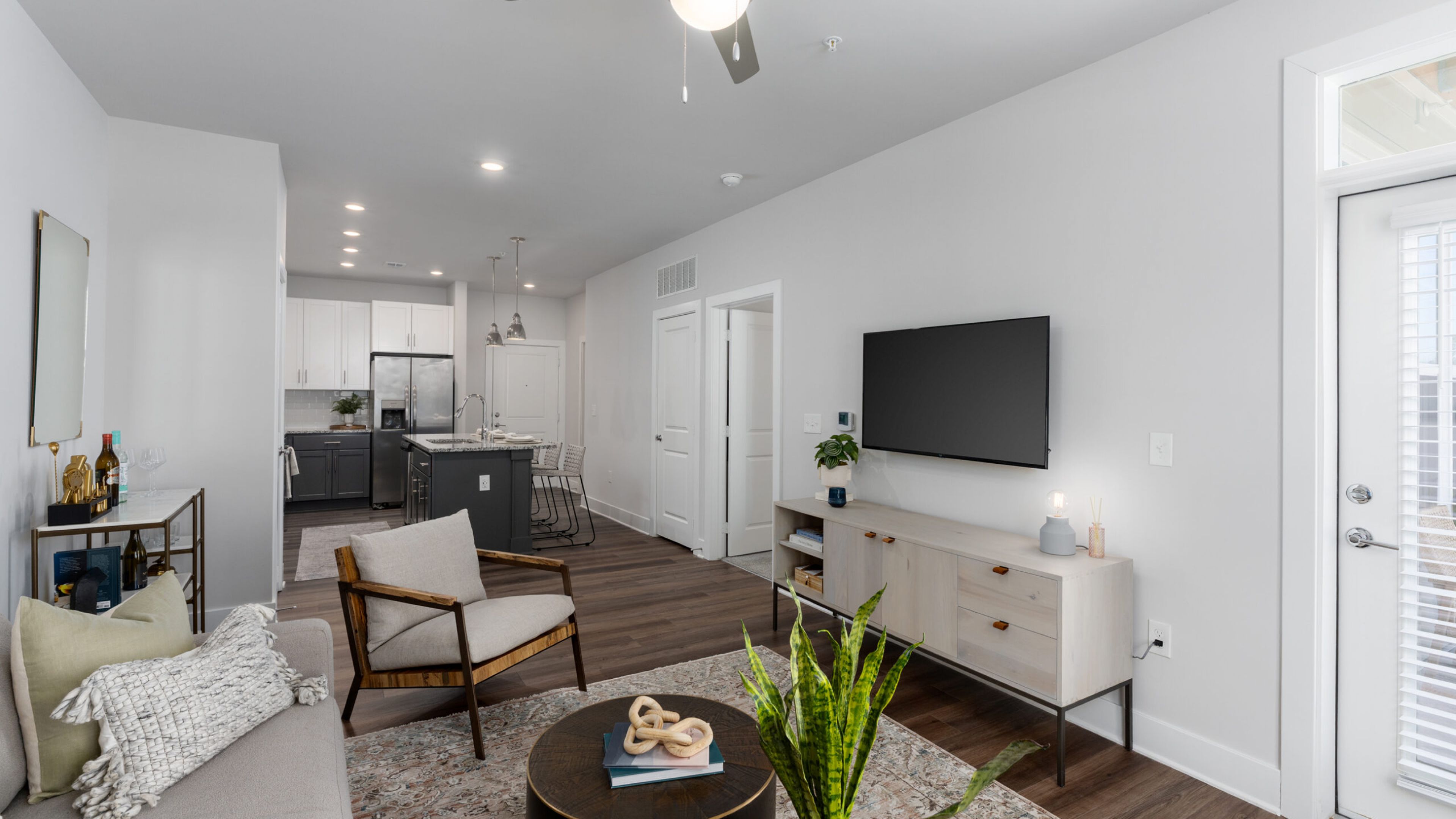Hawthorne at New Bern modern kitchen with granite island, white cabinets, bar stools, and view into a bright living room with blue curtains.