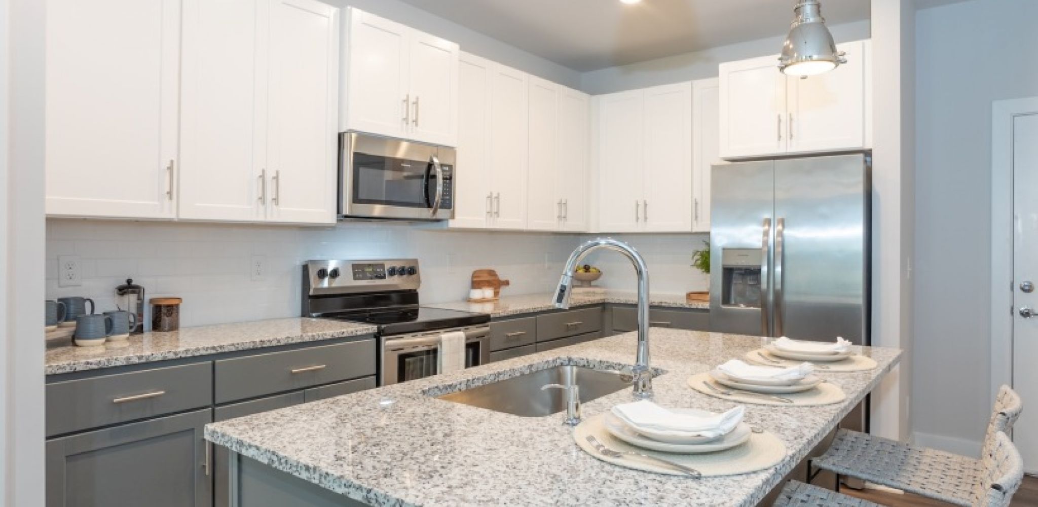 Hawthorne at New Bern modern kitchen with white cabinets, stainless steel appliances, and a granite island set for four.